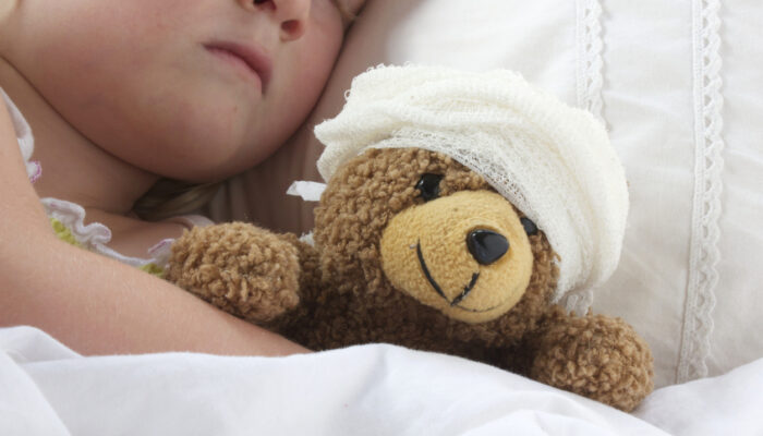 Young girl poorly in bad cuddling her teddy who also feels poorly.